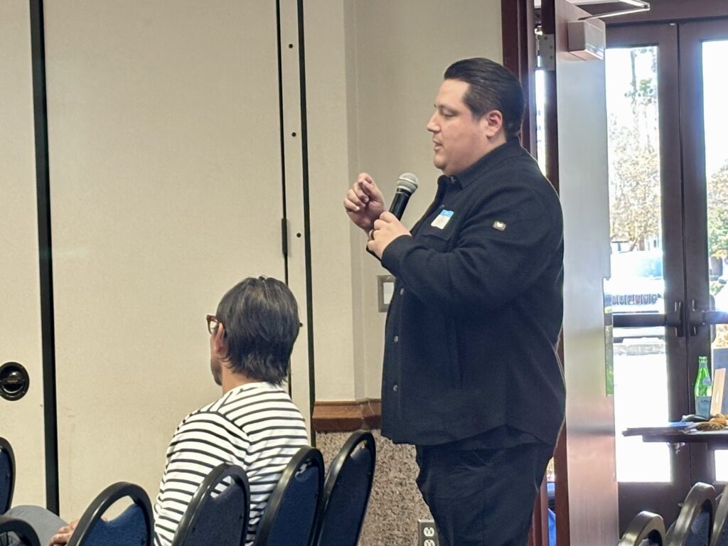 Bob Lozano habla por un micrófono mientras se encuentra de pie entre los asistentes sentados durante una reunión pública del sector de la restauración.