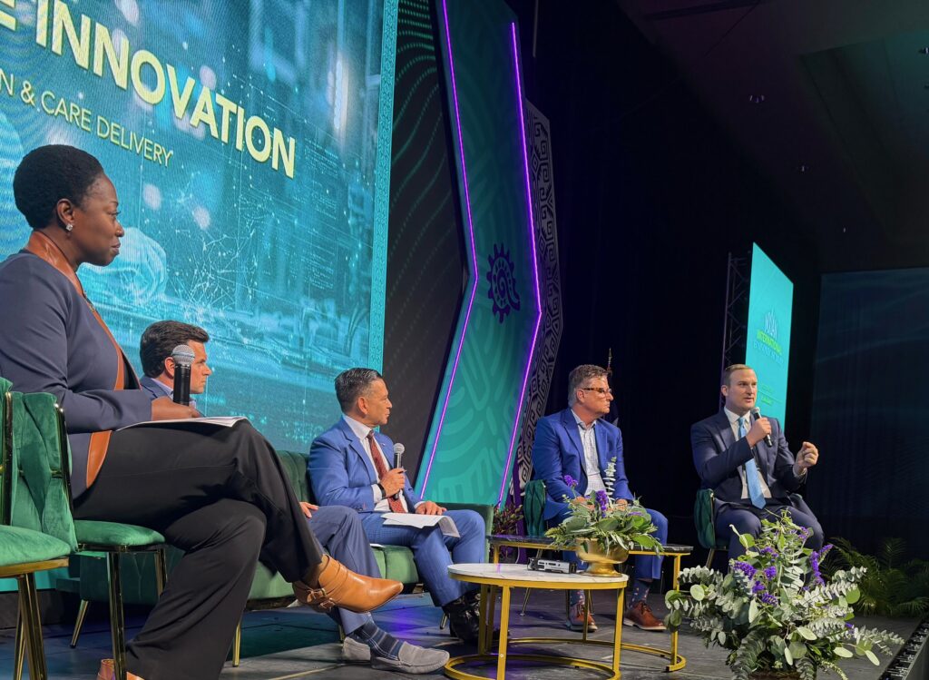 Speakers participate in a panel discussion on artificial intelligence and innovation in healthcare during the MXLAN Economic Summit in McAllen, seated on stage with microphones and a digital screen backdrop.
