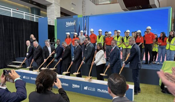 A group of local officials, business leaders, and workers wearing hard hats participate in a ceremonial groundbreaking for a new manufacturing plant in McAllen, holding shovels on a stage with Valeo branding in the background.