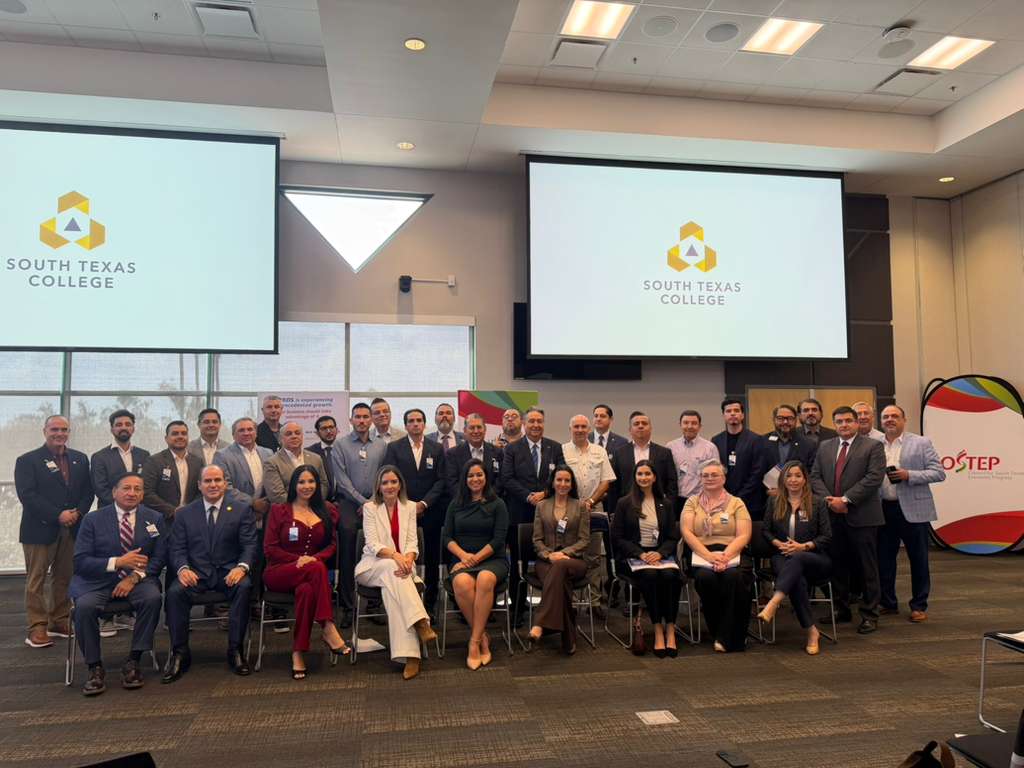 A large group of business leaders and officials pose for a photo inside a conference room at South Texas College during a manufacturing data presentation event.