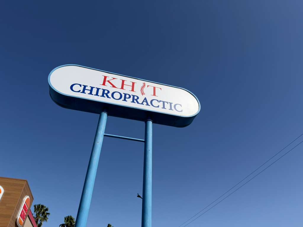 Un alto cartel al borde de la carretera en el que se lee el nombre «Khit Chiropractic» contra un cielo azul claro.