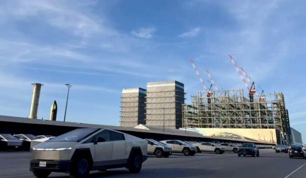 Vehicle driving on State Highway 4 toward SpaceX Starbase facilities in Boca Chica, with industrial structures visible in the distance under a blue sky.