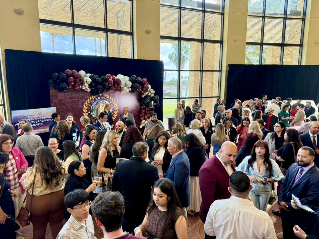 A large group of attendees gathers in a bright lobby space, talking and networking during a formal event reception.