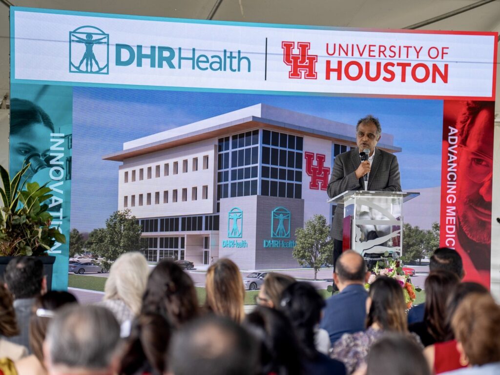 El Dr. Manish Singh pronuncia un discurso desde el estrado durante la ceremonia de inicio de las obras de un centro de investigación médica y formación de DHR Health y la Universidad de Houston.