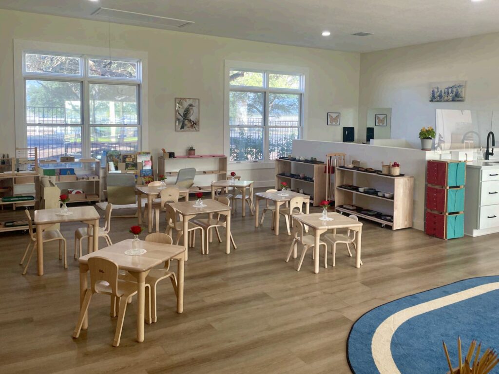 Interior de un aula de la escuela Ad Astra, con pequeñas mesas y sillas de madera, estanterías abiertas y grandes ventanas que dejan entrar la luz natural.