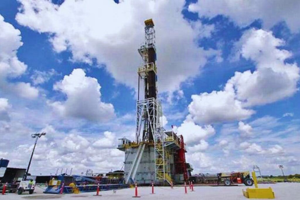Una gran plataforma de perforación de petróleo y gas se alza en un terreno industrial llano, bajo un cielo parcialmente nublado.