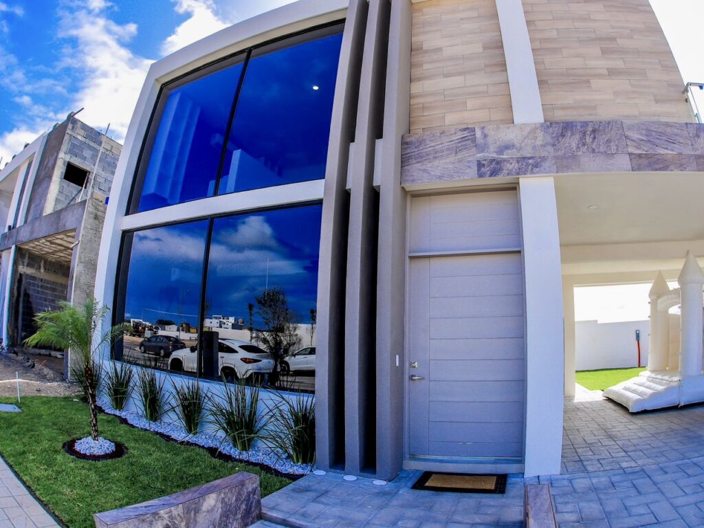 Una vivienda moderna de dos plantas con grandes ventanales y una entrada cubierta, con un pequeño jardín y obras en las inmediaciones.
