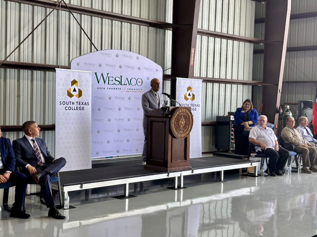 State Rep. Armando “Mando” Martinez speaks at a podium during an event announcing a new avionics training program inside an airport hangar.