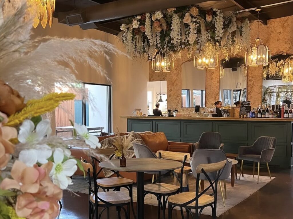 Zona de asientos y comedor en el interior de un establecimiento de Southern Roots Market, con decoración floral y mesas de cafetería.