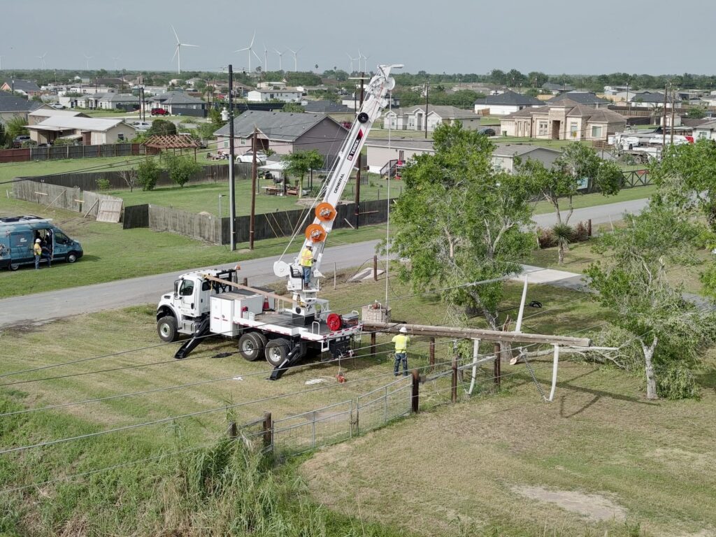 Utility crews and trucks repair a damaged power pole in a residential area following severe weather.