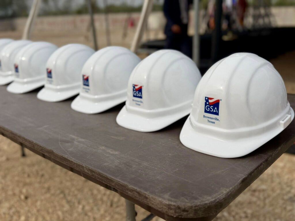 Cascos de obra blancos con el logotipo de la GSA alineados sobre una mesa antes de la ceremonia de inicio de las obras del puente Gateway International en Brownsville.