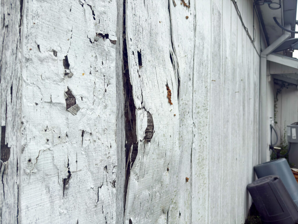 Rotting lower wall panels and deteriorated wood siding outside the aging VFW Post 2410 building.