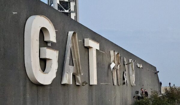 Damaged Starbase gateway sign with missing and bent letters near launch infrastructure.