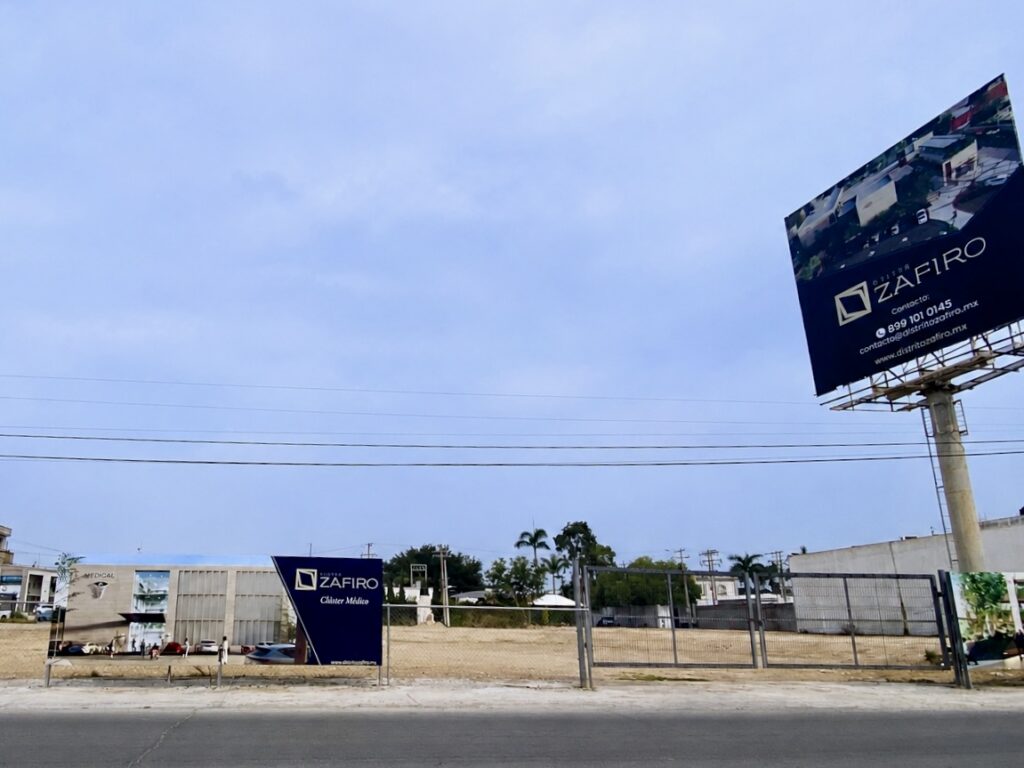 Empty development site in Reynosa with Distrito Zafiro project signage and a billboard near a major roadway.