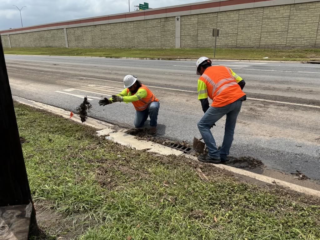 Dos trabajadores del Departamento de Transporte de Texas retiran escombros de un desagüe pluvial situado al borde de la carretera durante las operaciones de respuesta ante las inundaciones.