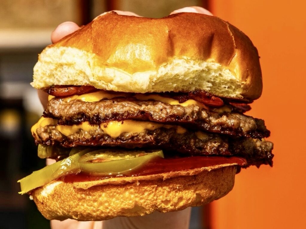 Primer plano de una minihamburguesa de queso con queso, pepinillos y salsa sobre un panecillo tostado.