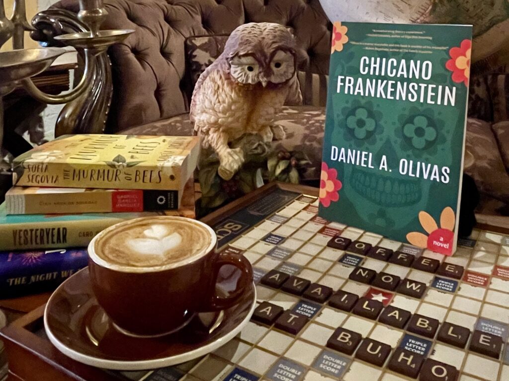 En la librería Búho hay un café con leche junto a una pila de libros, un tablero de Scrabble y una figurita de un búho.