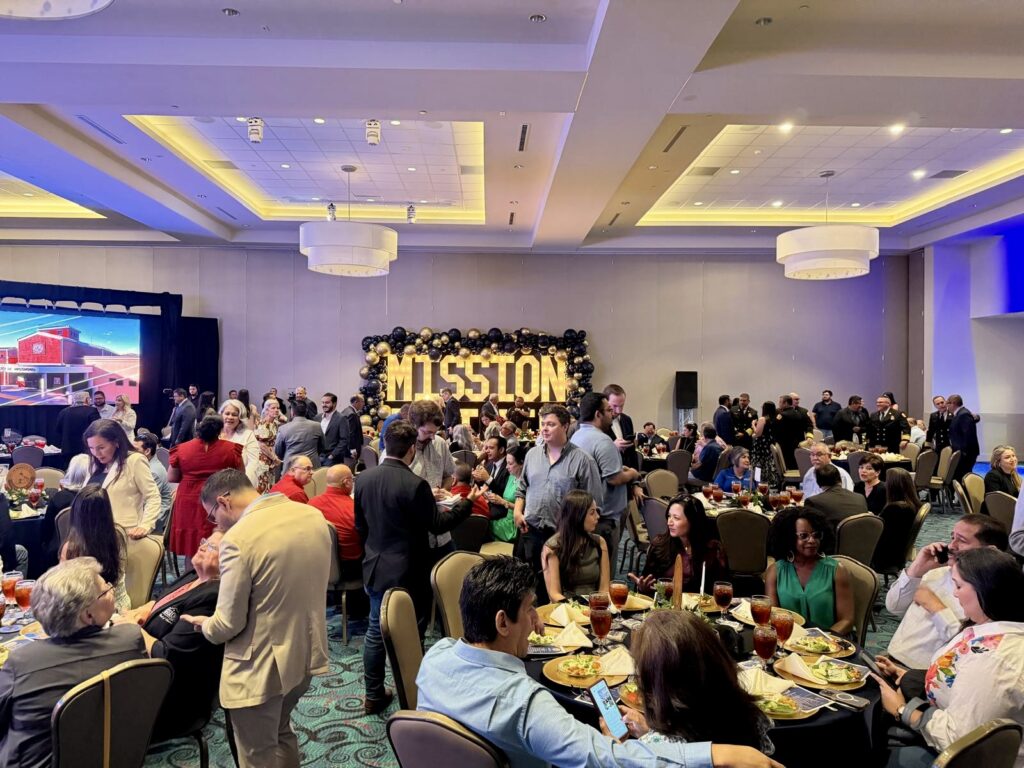 Attendees gather inside the Mission Event Center before the City of Mission’s 2026 State of the City address, with a large illuminated “Mission” display in the background.