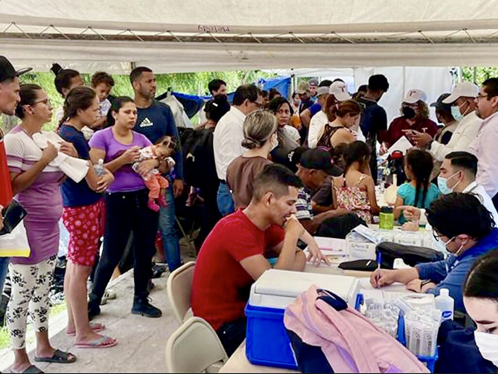 Families and other returned Mexican nationals gather around assistance tables at a crowded reception site in Matamoros.