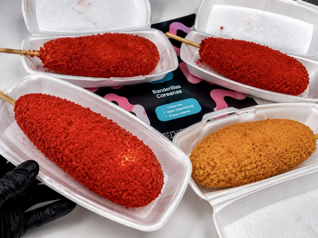 Korean corn dogs from Banderillas Coreanas Buck’s are covered in red and orange crunchy toppings and served in takeout containers.