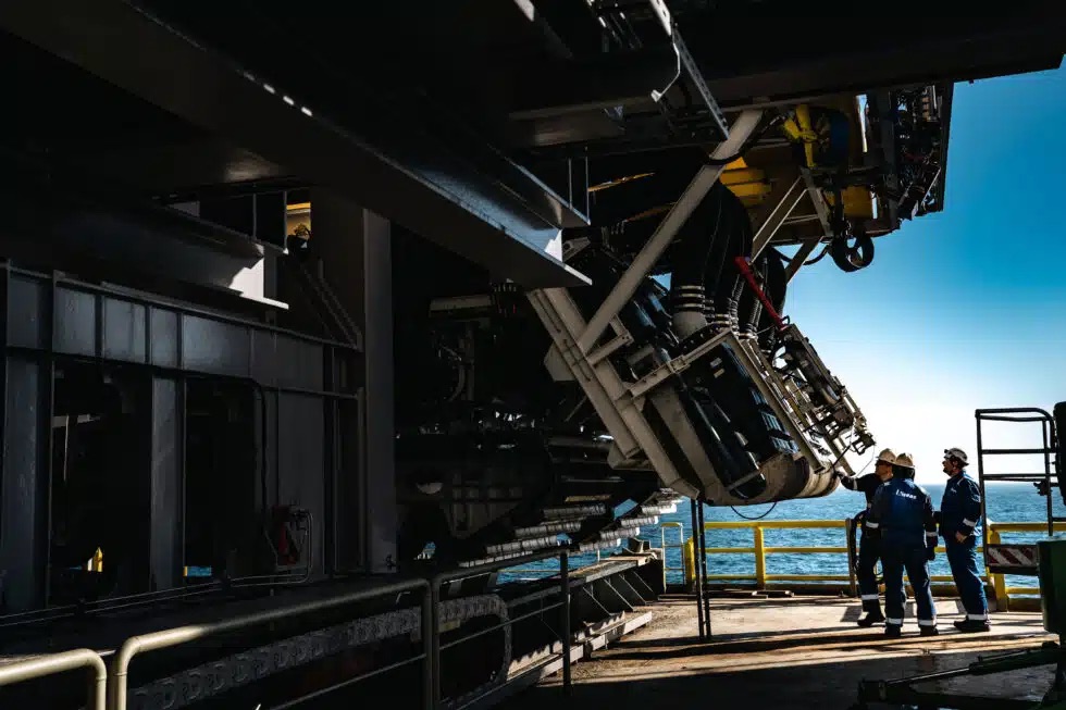 Workers stand beside large deep-sea nodule collection equipment aboard a vessel.