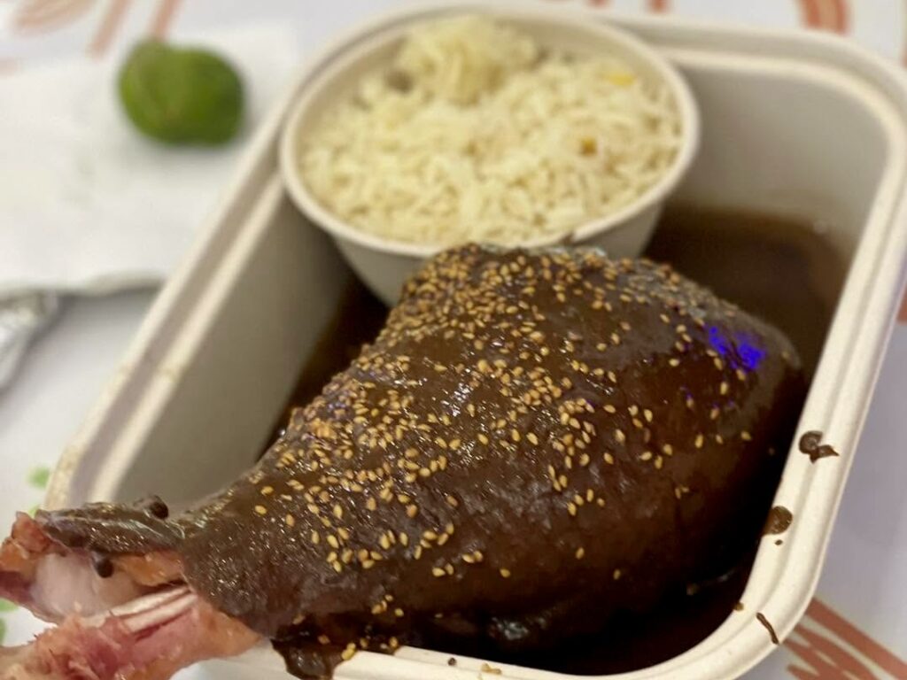 A prepared dish covered in dark mole sauce and sesame seeds sits beside a serving of rice.