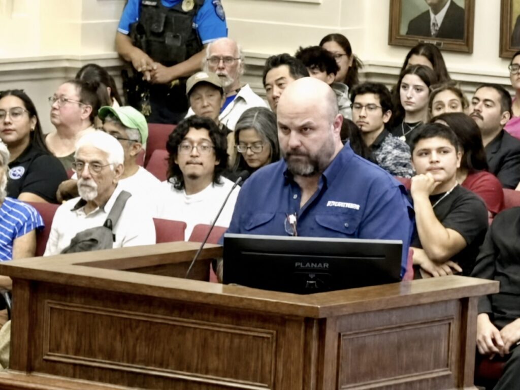 Eliud Cavazos, wearing a blue button-down shirt, speaks at a podium during a Brownsville City Commission meeting.